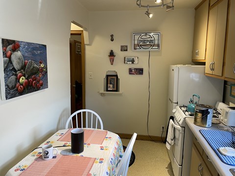 A kitchen with a table and chairs in the foreground and a refrigerator, oven, and washing machine in the background.