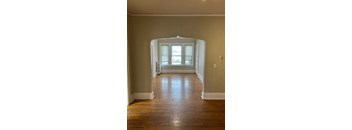 A room with a wooden floor and a white archway leading to a window.