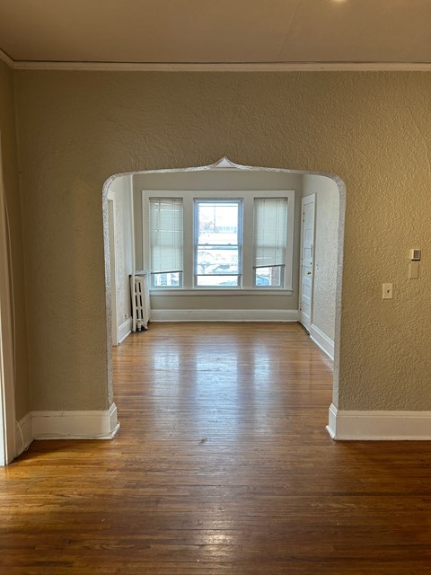 A room with a wooden floor and a white archway leading to a window.