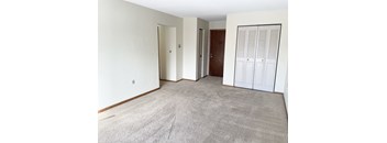 A room with a grey carpet and white walls with a door and a wardrobe.