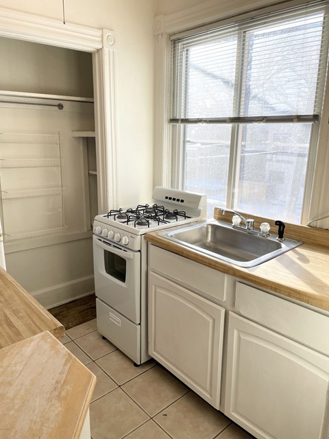 A white kitchen with a stove, sink, and cabinets.