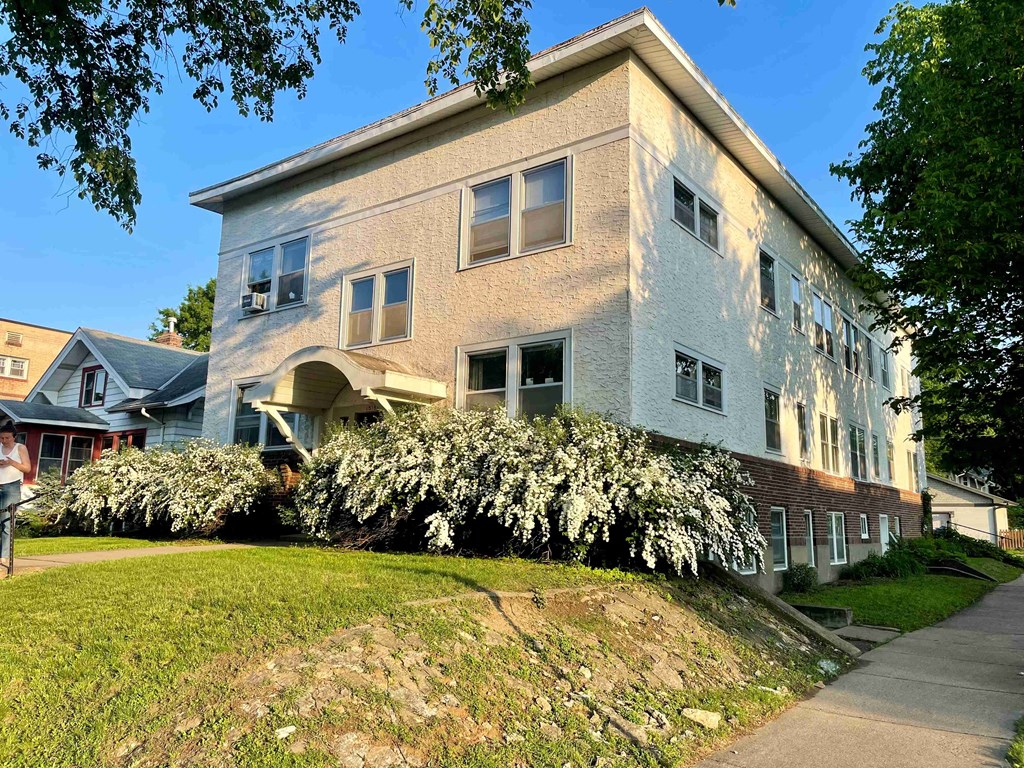 A two-story building with a white exterior and a large bush in front of it.