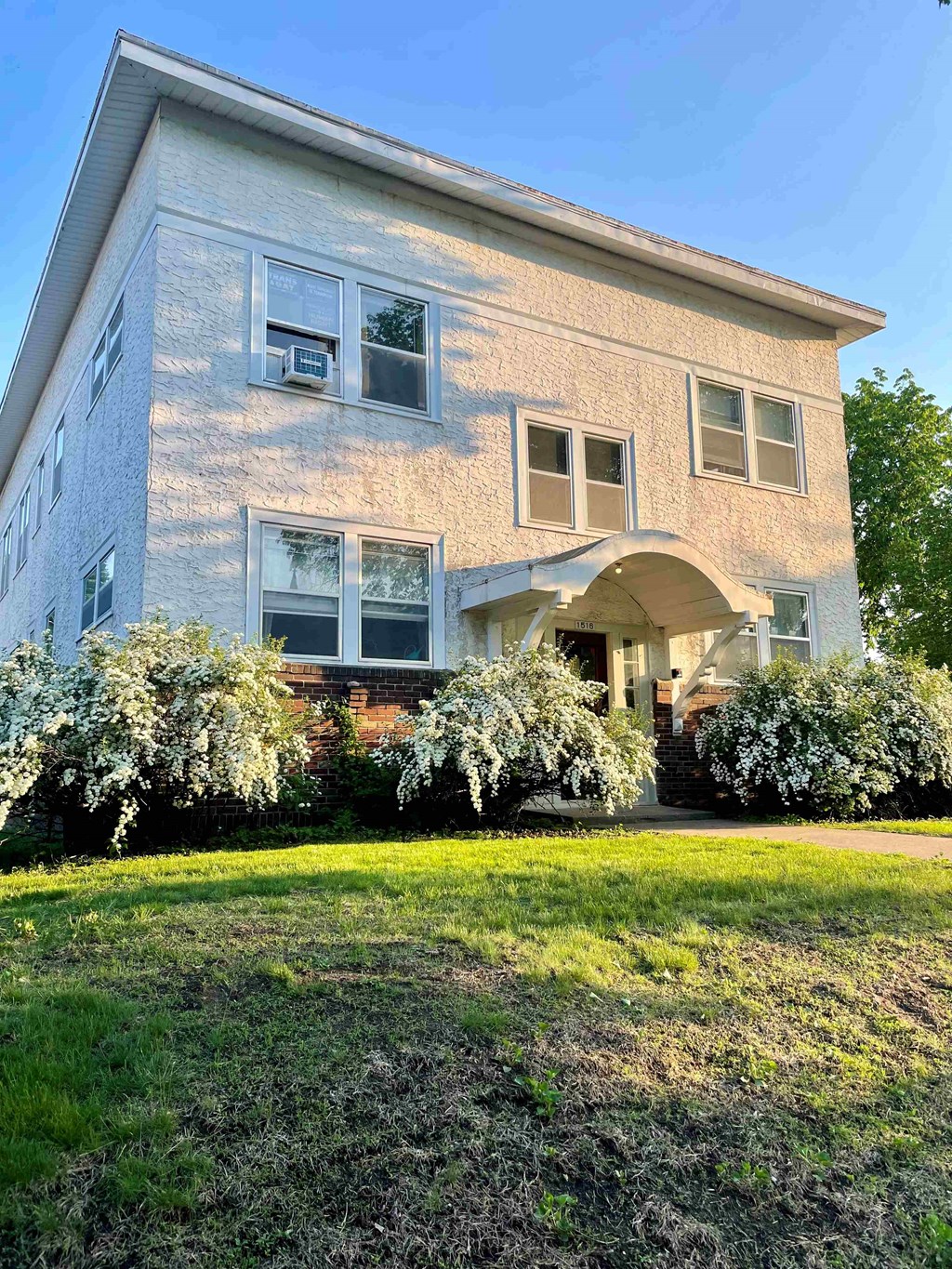 A house with a white and beige exterior and a green lawn in front.