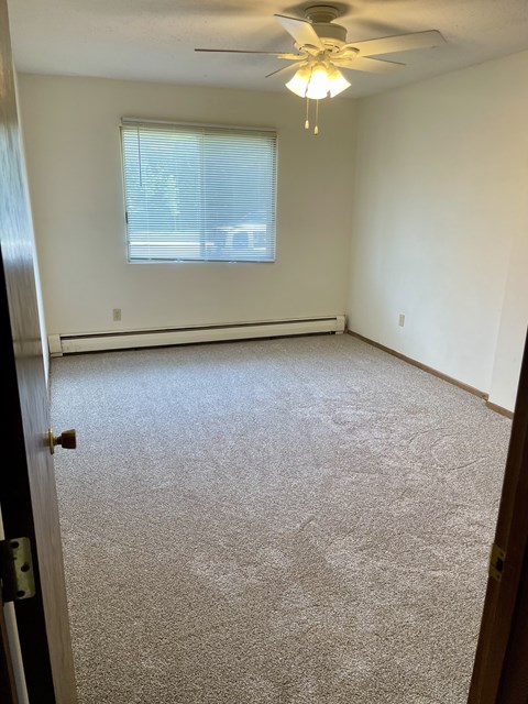A room with a carpet floor and a ceiling fan.