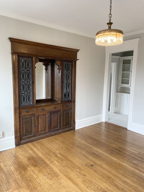 A wooden cabinet with glass doors is in the middle of a room with a chandelier hanging from the ceiling.