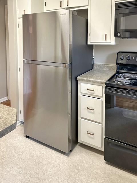 A silver refrigerator stands next to a black oven in a kitchen.