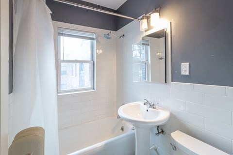 A white sink in a bathroom with a white tub and a window.