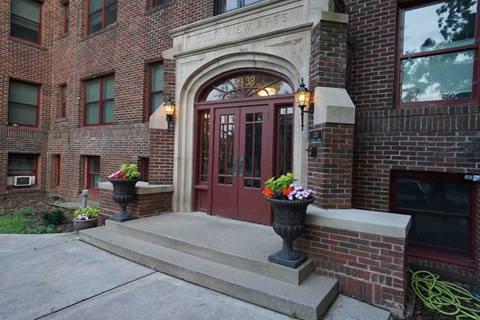 A red door is flanked by two large planters.