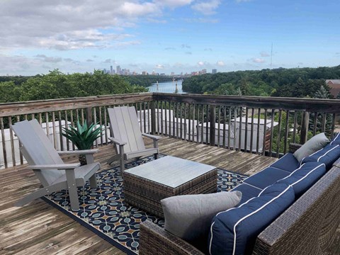 A wooden deck with a couch, chairs and a table with a view of a city skyline.