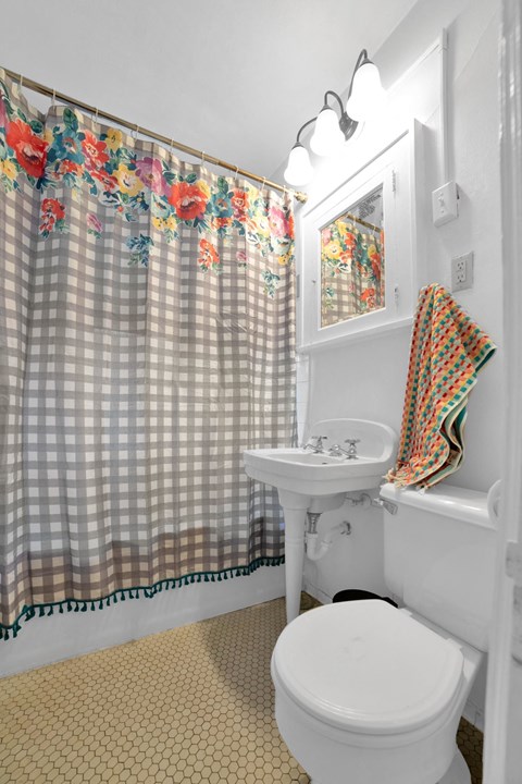 A white toilet sits under a shower curtain with a floral pattern.