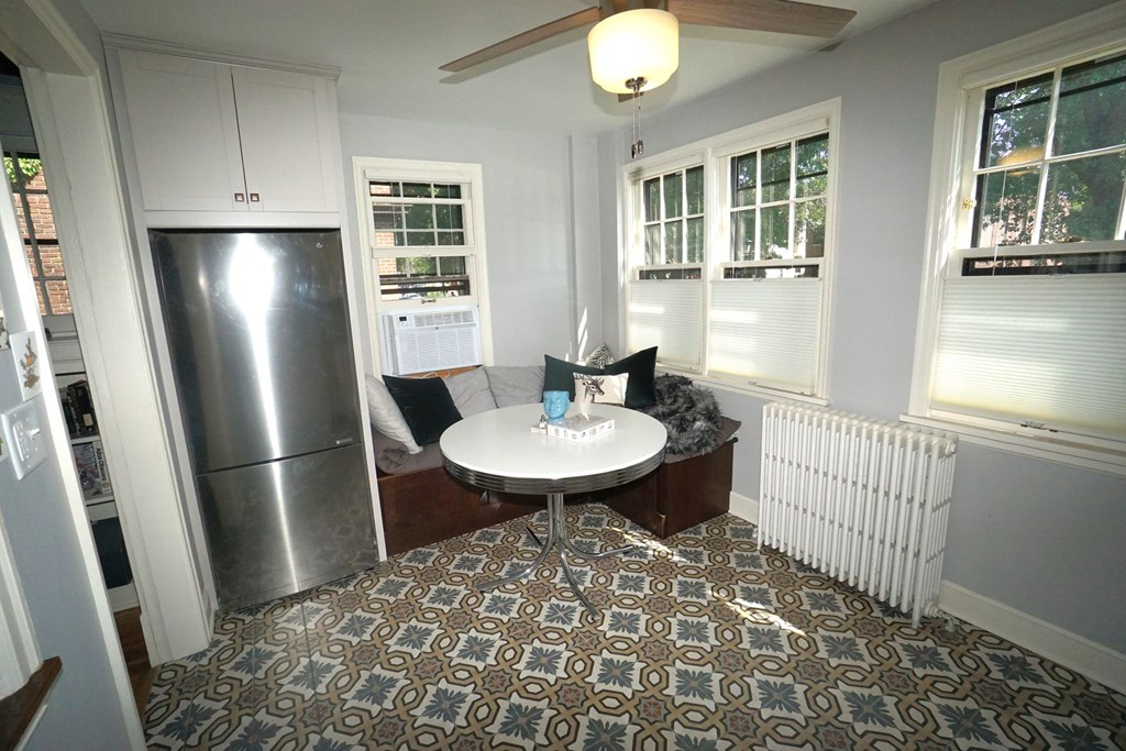 A kitchen with a refrigerator, a table with a white tablecloth and a ceiling fan.