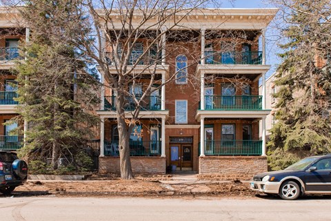 A tree in front of a brown building with a car parked in front of it.