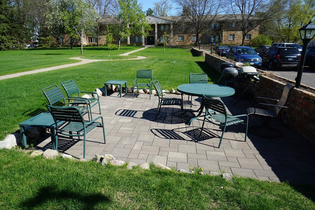 A sunny day at the park with green chairs and tables.