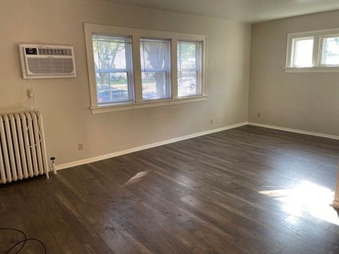 A room with wood flooring and two windows.