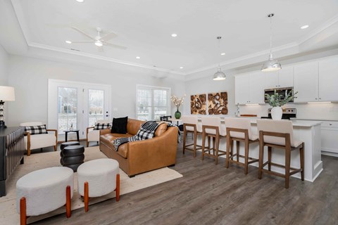 A modern living room with a brown sofa and a white kitchen in the background.