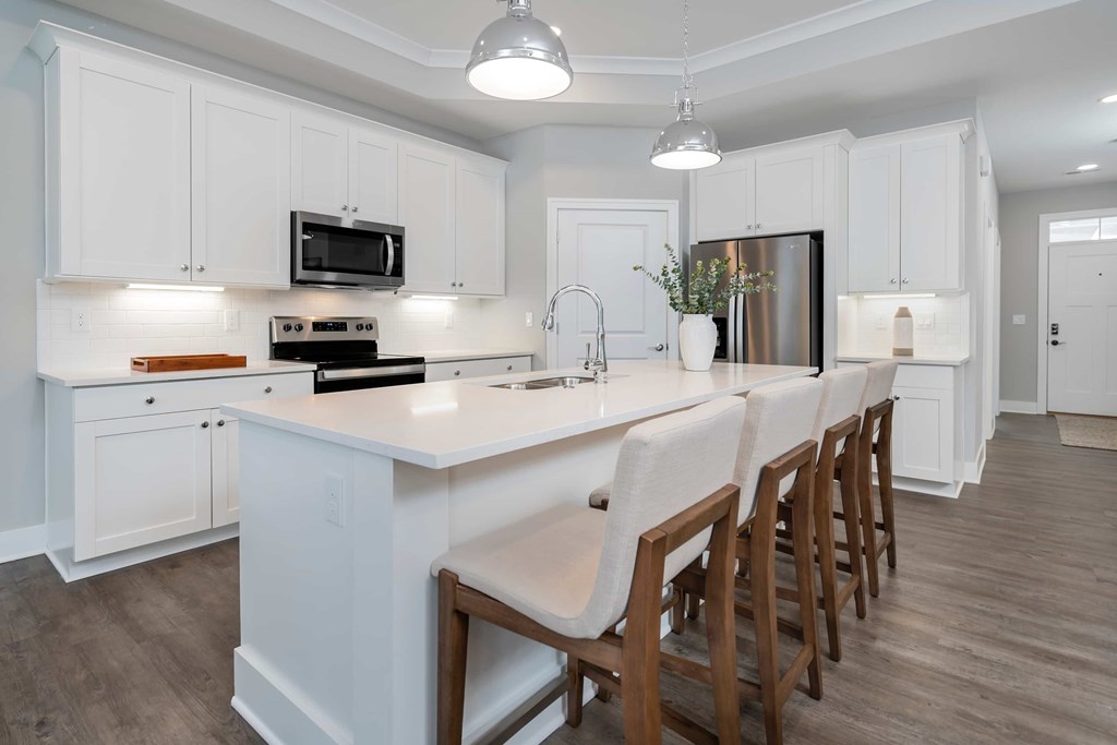 A kitchen with white cabinets and a long island with chairs.