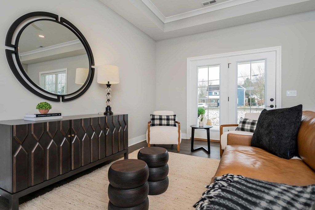 A living room with a brown leather couch and a round mirror on the wall.