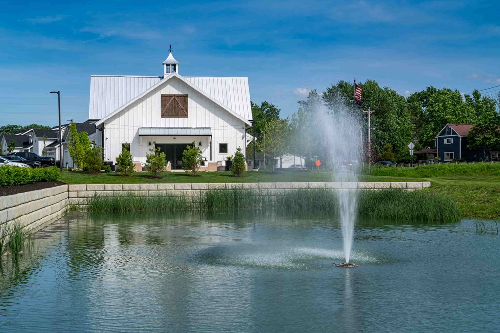 A white barn with a fountain in front of it.