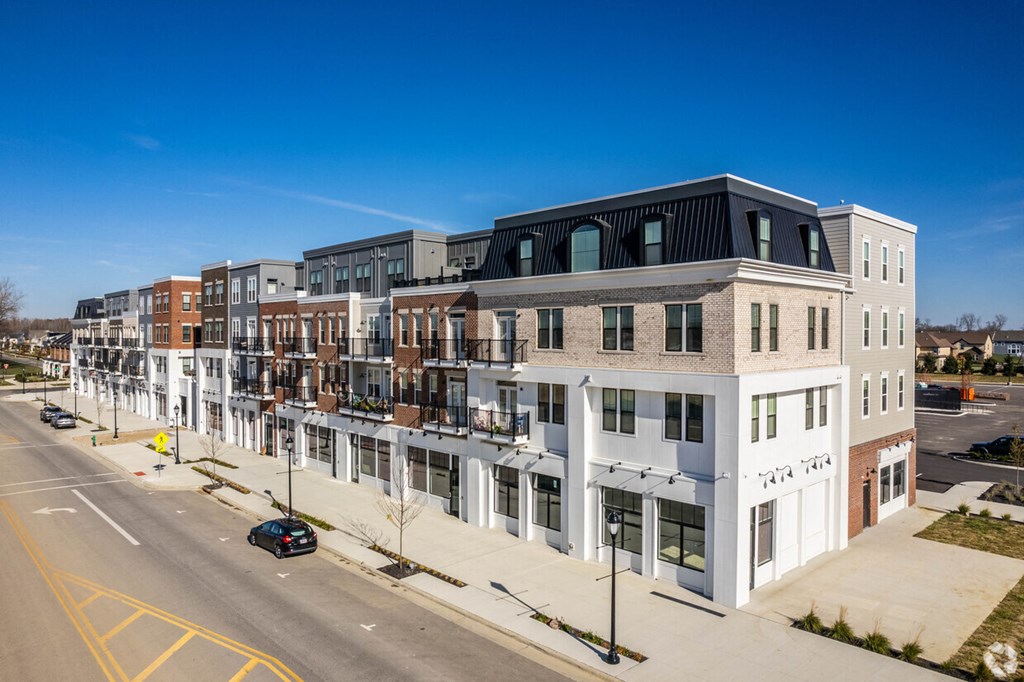 A street view of a row of modern buildings with cars parked on the side.