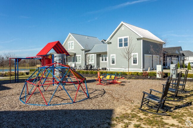 A playground with a red and blue swing set in front of a house.