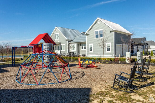 A playground with a red and blue swing set in front of a house.