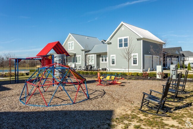 A playground with a red and blue swing set in front of a grey house.