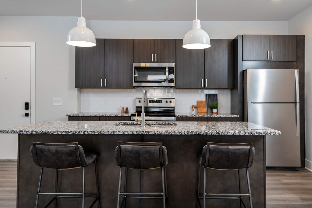 A modern kitchen with a granite countertop and bar stools.
