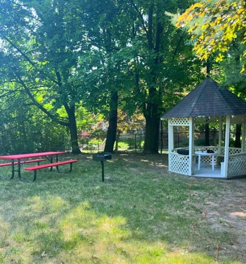 A gazebo sits in a grassy area with picnic tables and trees.