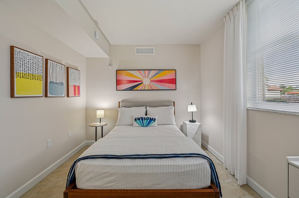 A bedroom with a bed, two lamps, and a painting on the wall.
