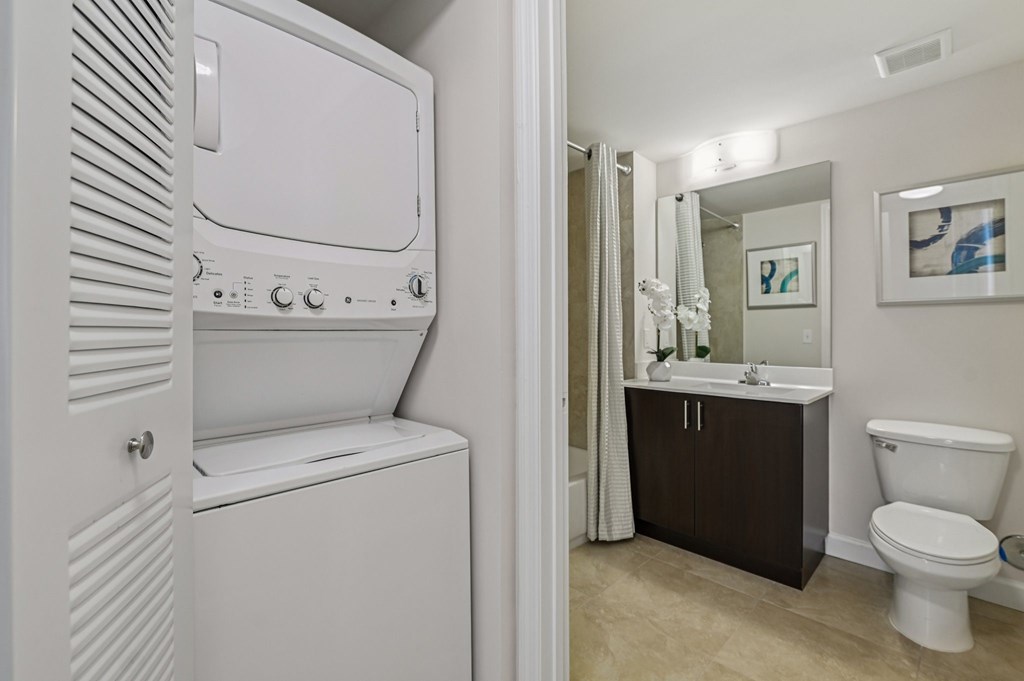 A white washing machine is in a bathroom with a toilet and sink.