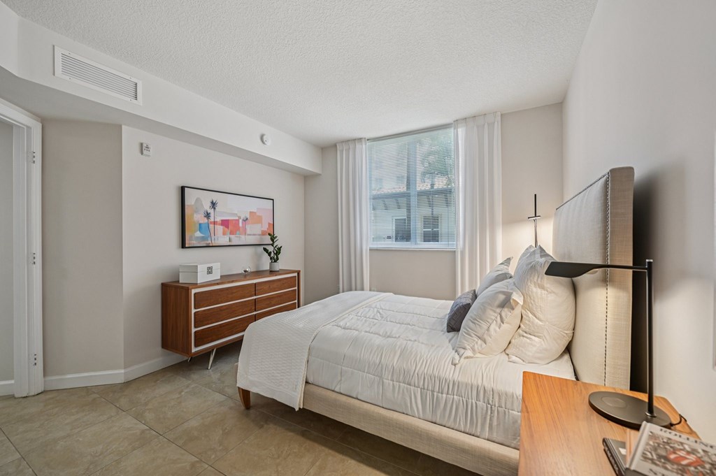 A bedroom with a large bed, a nightstand, and a window with curtains.