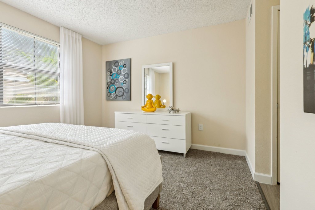 A bedroom with a white bed and a dresser with a mirror and a painting on the wall.
