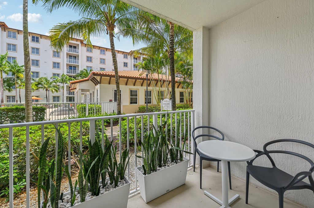 A balcony with a table and chairs overlooking a courtyard with plants.