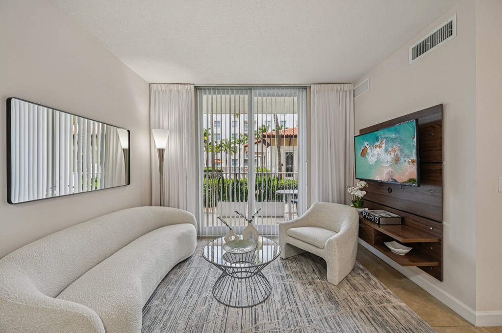 A living room with a white sofa, a glass table, and a television.