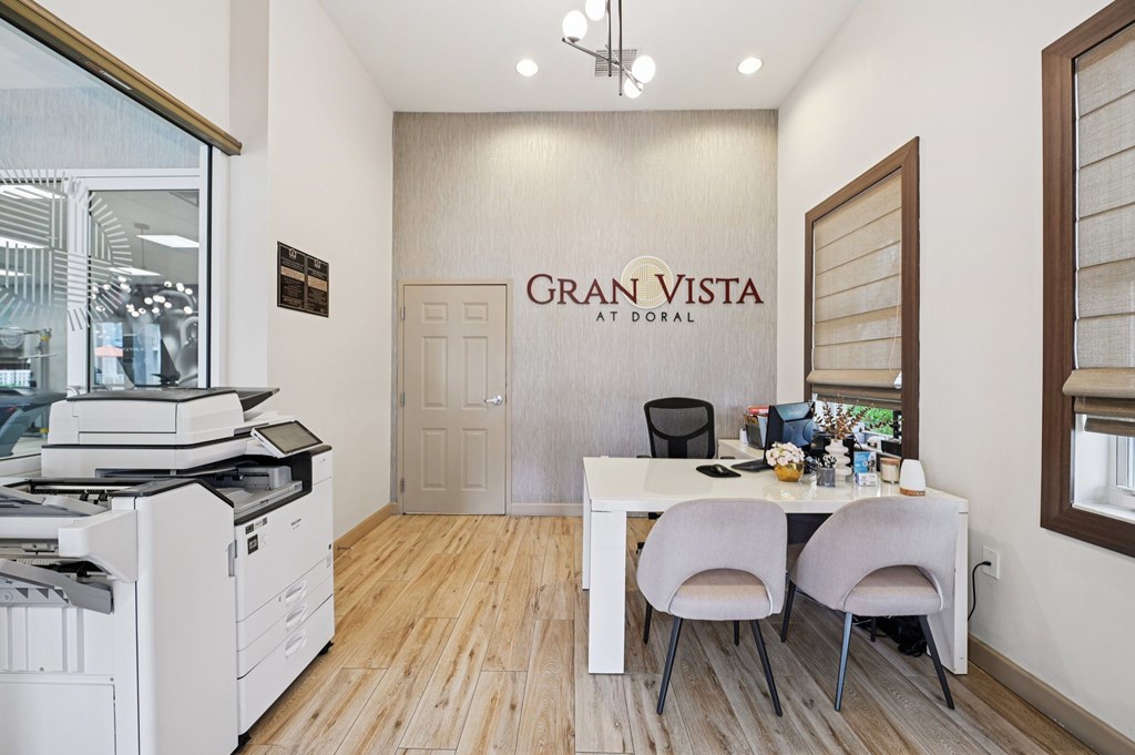 A white desk with two chairs and a printer in a room with a sign that says Gran Vista at Doral.