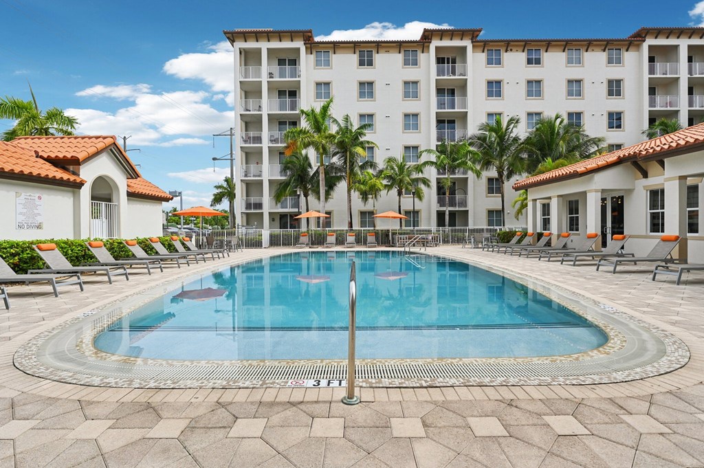 A large swimming pool in front of a hotel with a white building and palm trees.