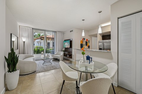 A modern dining room with a glass table and white chairs.