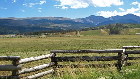 A wooden fence in a grassy field with mountains in the background.
