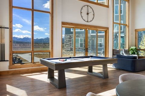A pool table in a room with a view of the mountains outside the window.