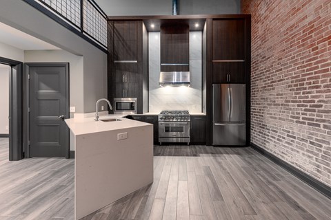 A modern kitchen with a brick wall and wooden floors.