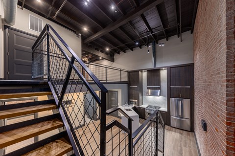 A staircase with a metal railing leads to a kitchen area.