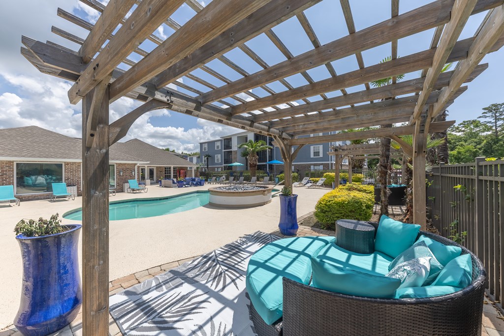 A wooden pergola over a patio with a wicker chair and a blue vase.