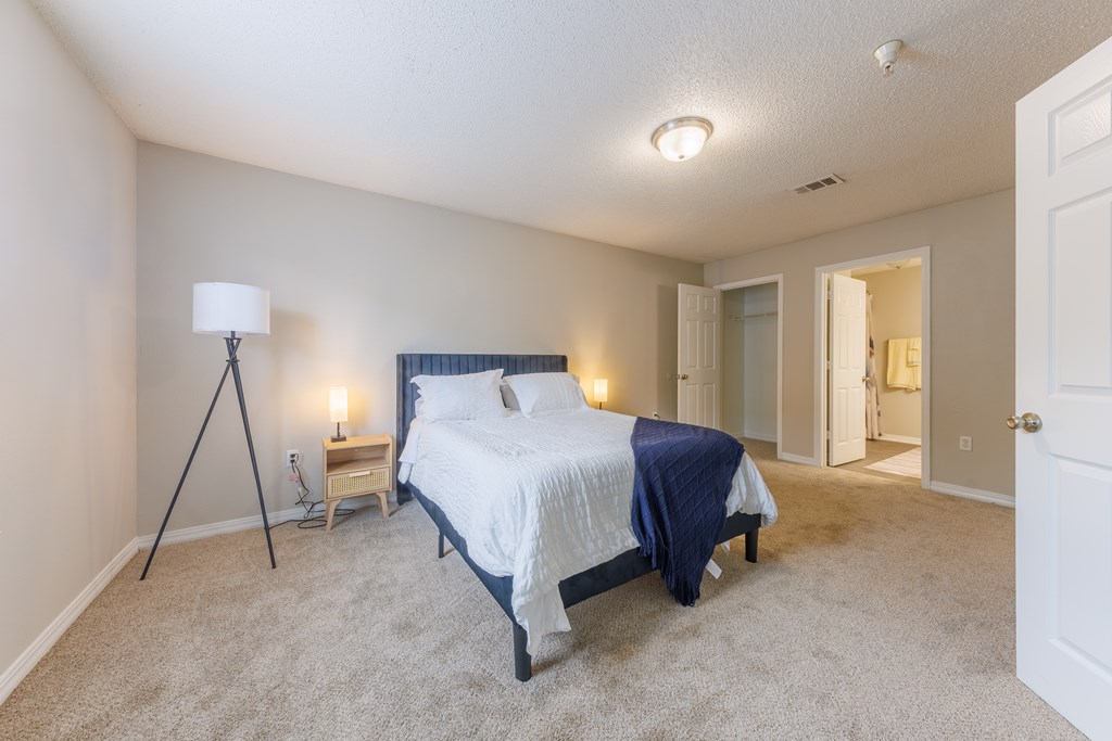 A bedroom with a bed, lamp, and carpet.