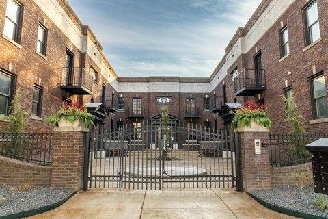 A gated entrance to a brick building with a metal gate and plants on either side.