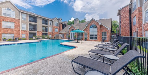 A pool surrounded by lounge chairs and a brick building.