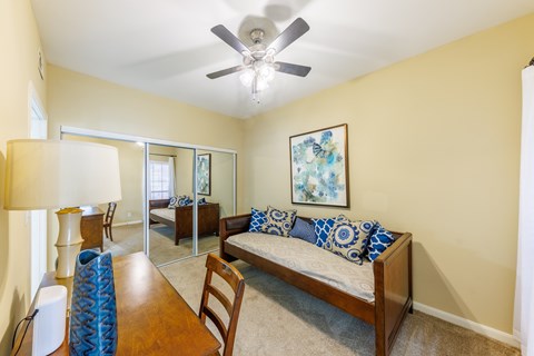 A bedroom with a bed, a chair, a table, and a ceiling fan.