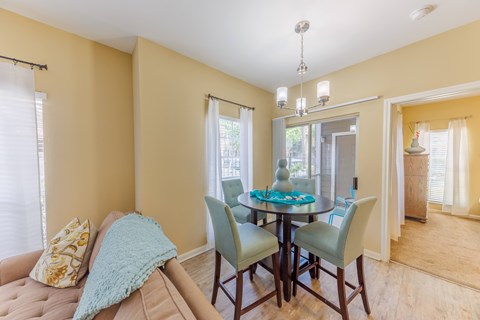 A dining room with a table set for four and a couch with a throw pillow.