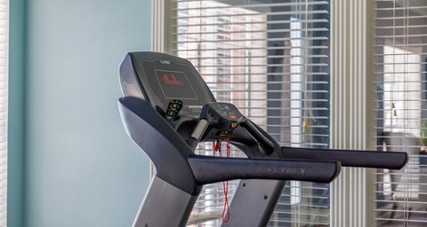 A treadmill with a digital display and control panel is placed in a room.