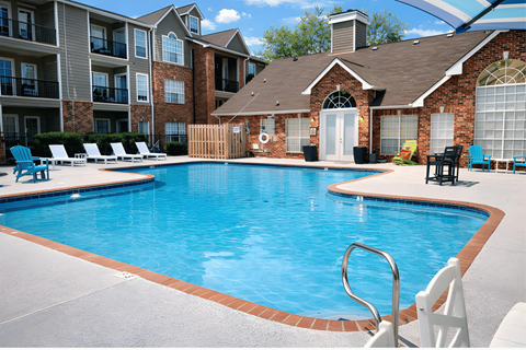 A swimming pool in front of a brick house with a white chair.