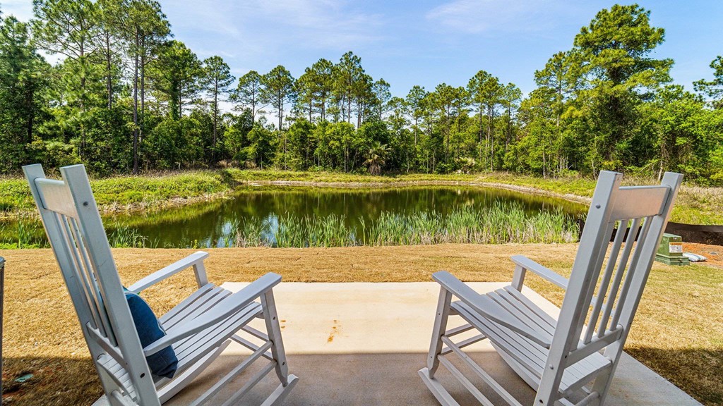 Two chairs are placed on a concrete slab with a pond and trees in the background.
